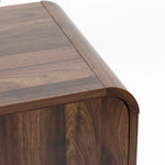 Close up view of the corner of a walnut TV stand with a smooth, rounded edge and visible wood grain.