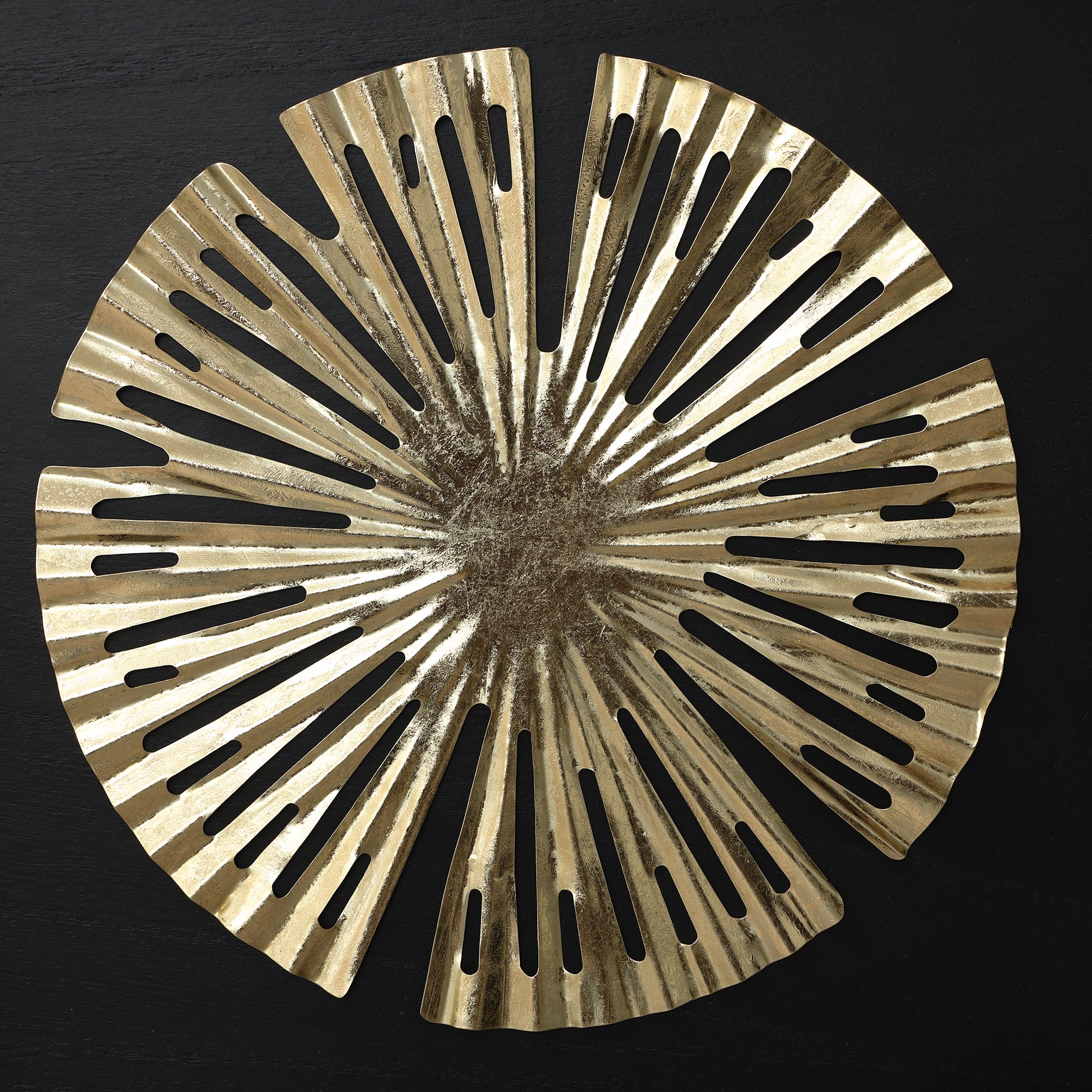 Circular metallic gold decorative object with radial cutouts and irregular edges.