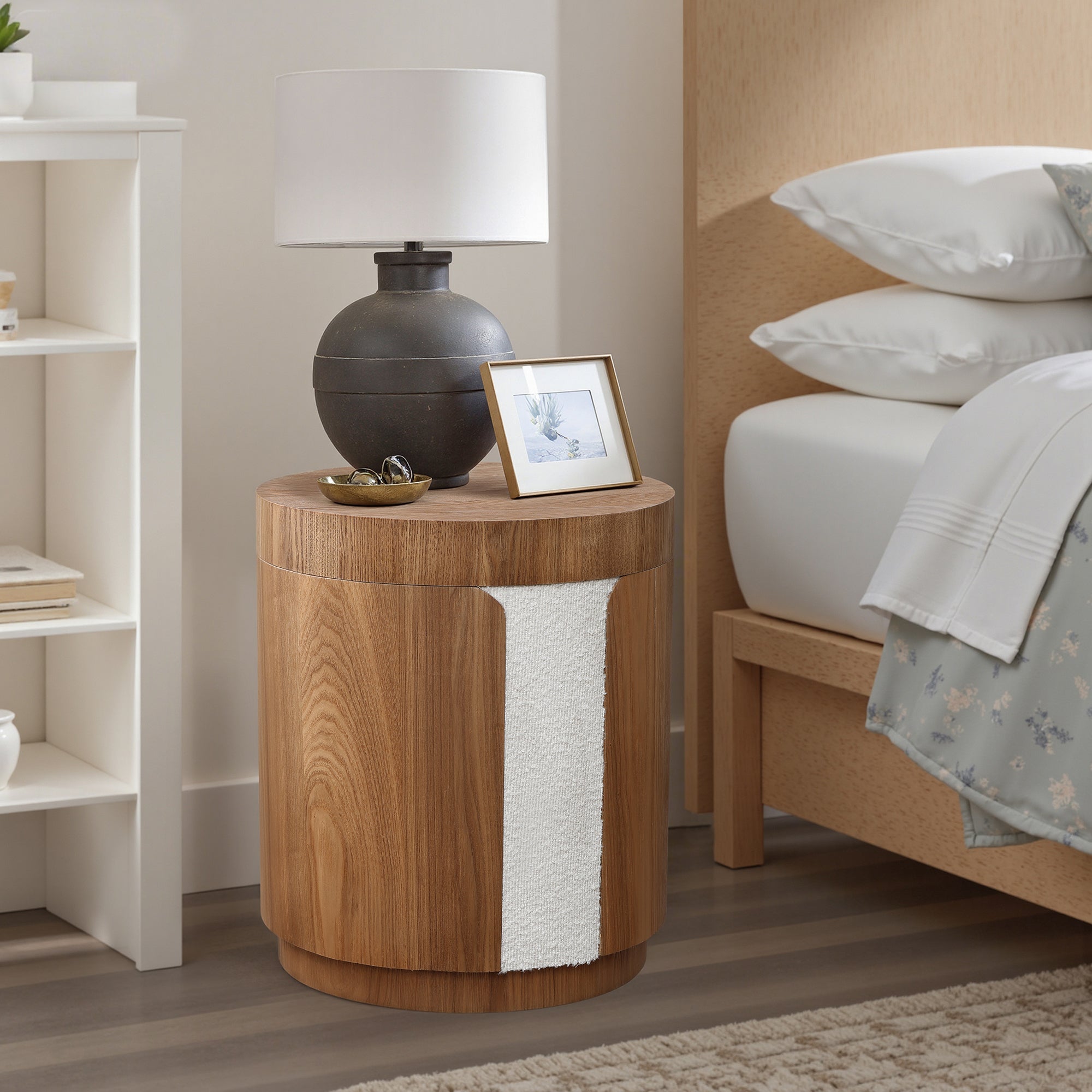 Round wood storage side table with a white accent holds a black lamp, framed photo, and small dish.