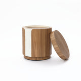 Cylindrical wooden container with a white textured vertical stripe and a matching round lid beside.