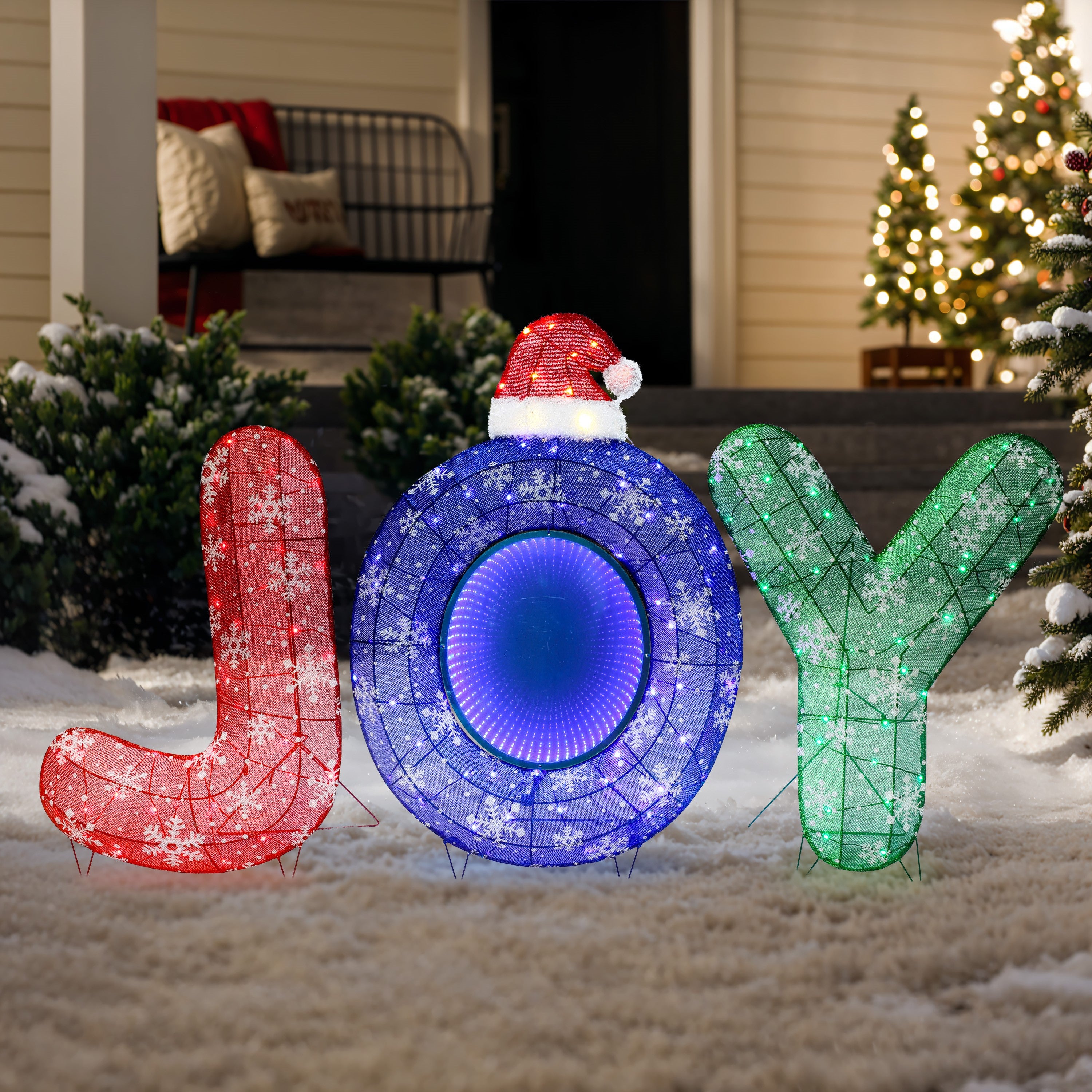 Large illuminated letters spelling JOY, with a Santa hat on the O, perfect festive photo moments on a snowy lawn.