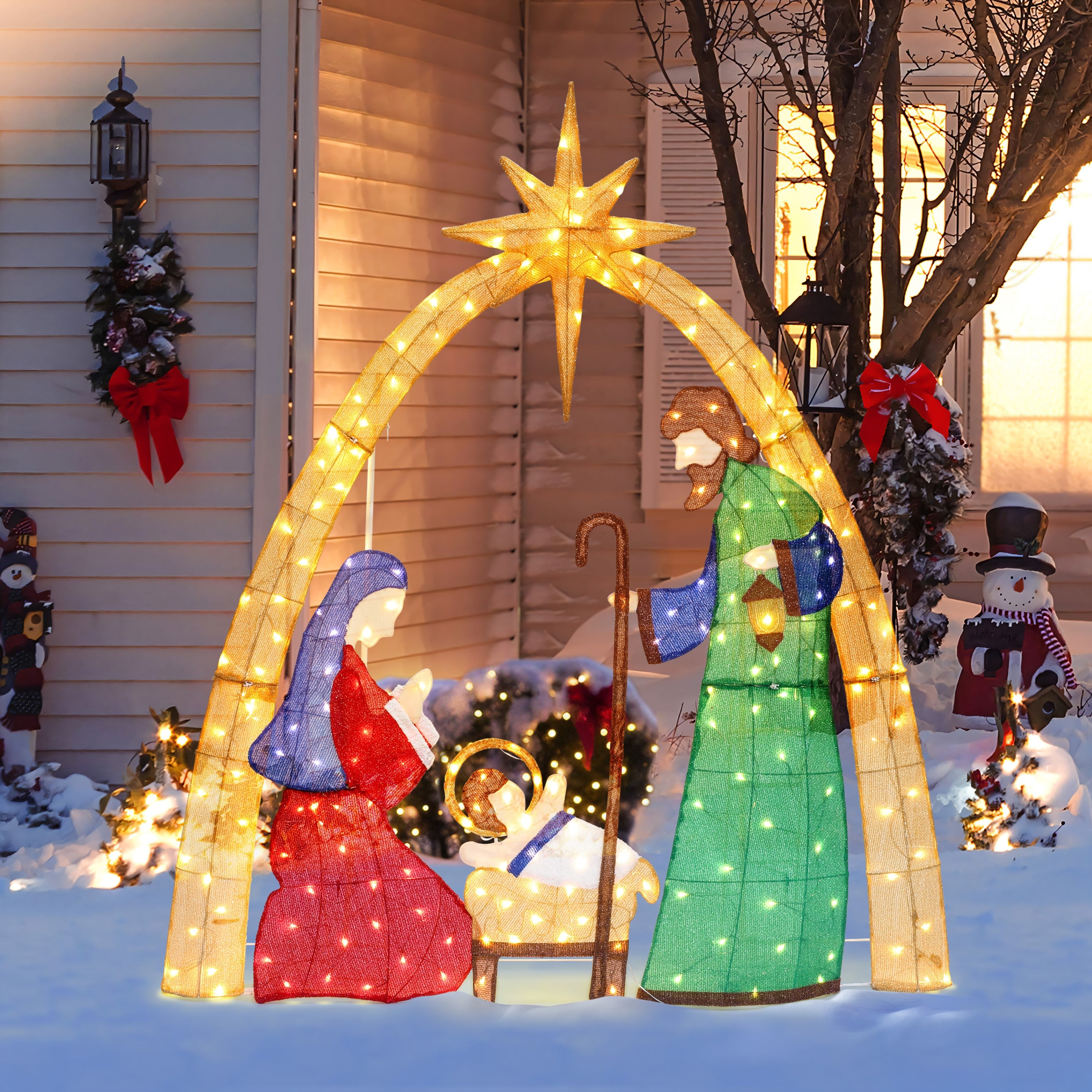 Illuminated nativity scene with Mary, Joseph, baby Jesus under lighted arch with star, displayed outdoors in snowy yard.