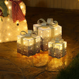 3 pre-lit gift boxes with silver bows are arranged on stone floor next to lighted snowman figure.