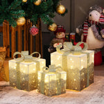 3 illuminated gift boxes with gold ribbons sit under decor christmas tree, plush snowman,bear figures in the background.