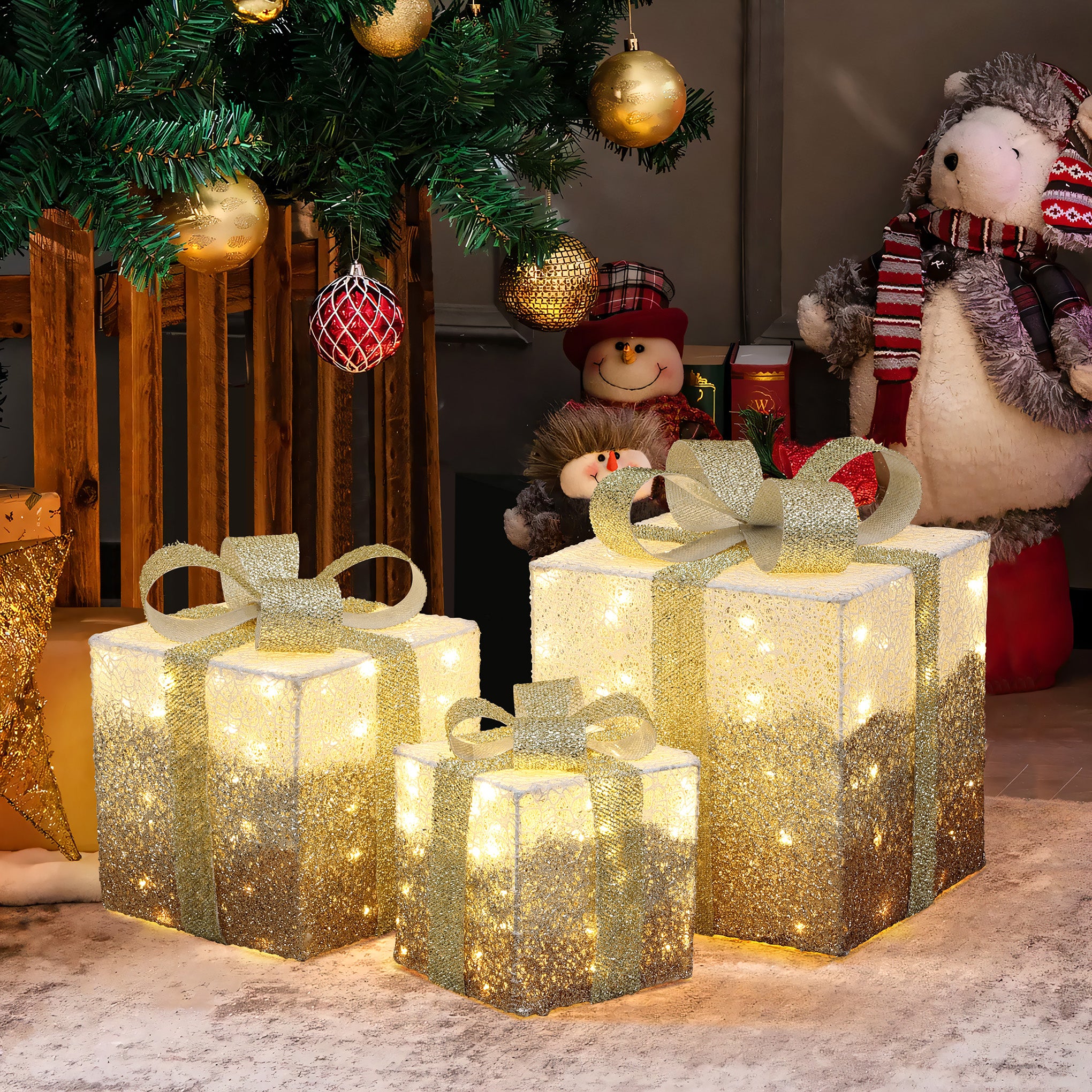 3 illuminated gift boxes with gold ribbons sit under decor christmas tree, plush snowman,bear figures in the background.