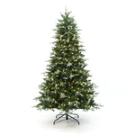 Pre-lit christmas tree with white lights stands on black metal stand against white background.