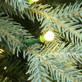 Close-up of lit white bulb on a green wire clipped to the frosted needles of pre-lit Christmas tree.