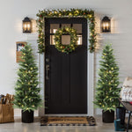 Black front door decor with lit wreath, garland is flanked by 2 christmas trees; a Merry Christmas doormat to the porch.