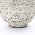 Close-up of the lower portion of a textured cement vase, showcasing its rough, speckled surface.