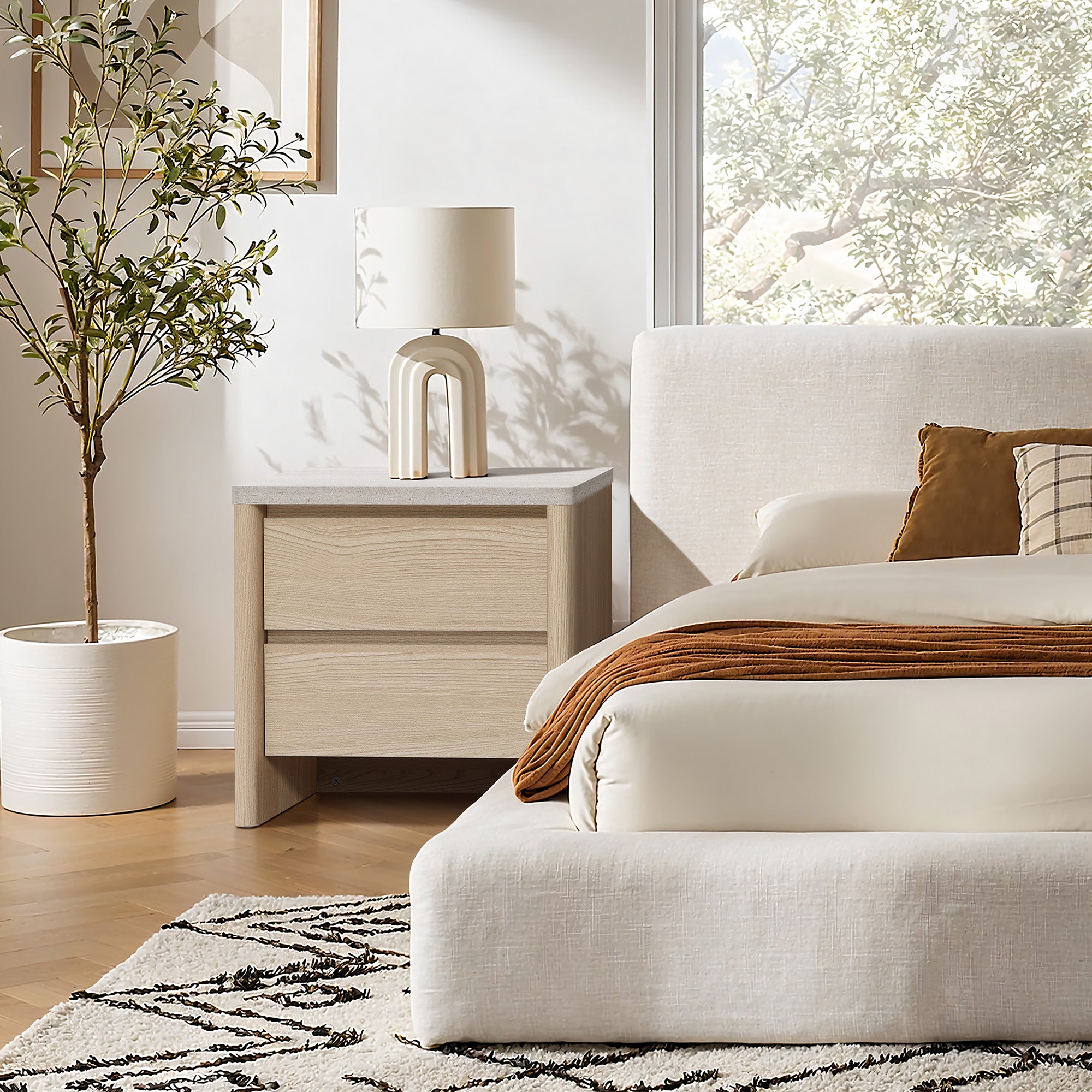 Modern bedroom with a wooden modern end table with a lamp, a potted plant, and a patterned rug.