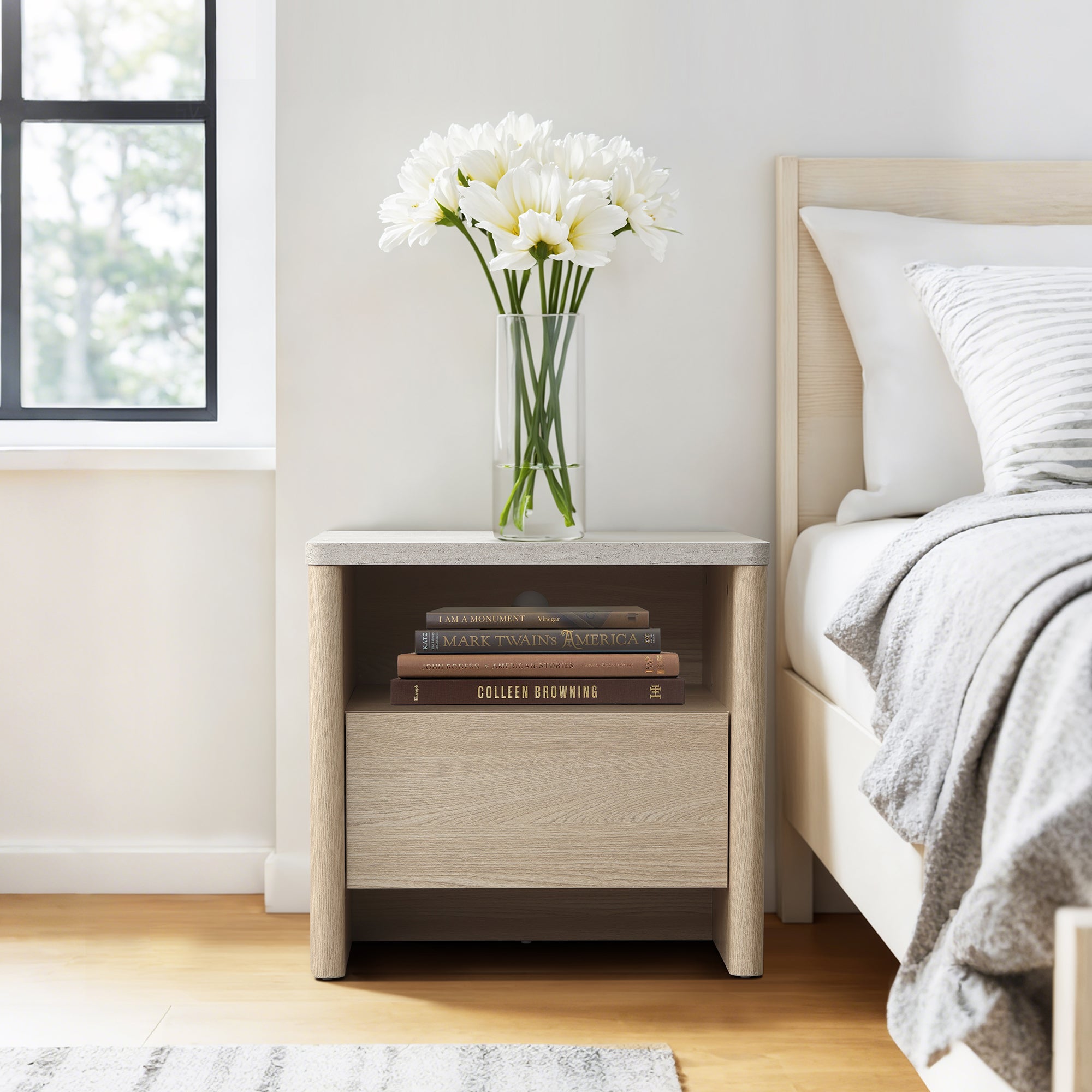 Snow oak end table with storage holds a vase of white flowers, three books on its shelf, and stands beside a neatly made bed.