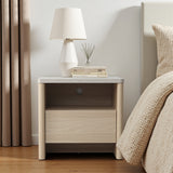 Modern snow oak end table with a drawer, holding a white lamp, stacked books, a reed diffuser, sits next to a beige bed.