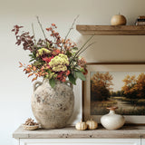 A large Terracotta Vase with autumn foliage sits on the floor next to a cream-colored sofa with patterned pillows in a cozy farmhouse living room.