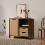Console cabinet with woven rattan doors and drawers, decorated with a framed feather print, a glass vase of flowers, and stacked books.