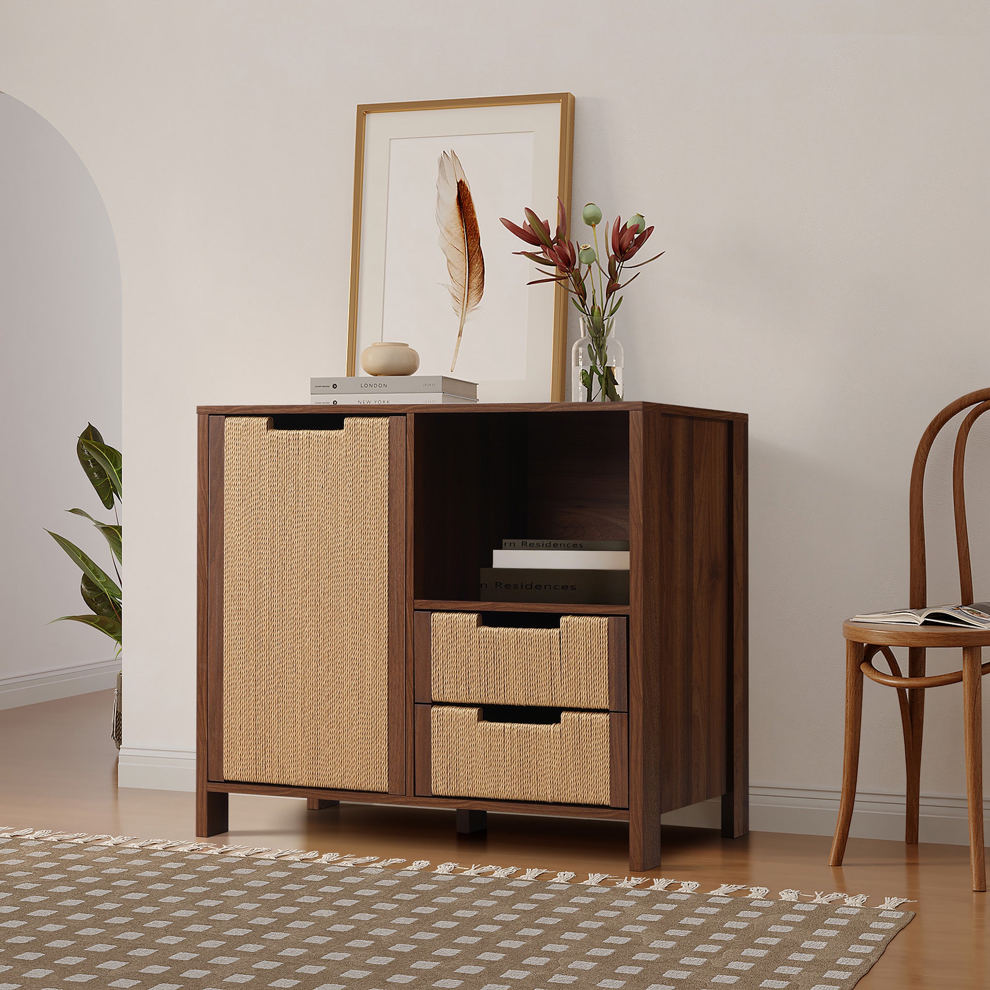 Console cabinet with woven rattan doors and drawers, decorated with a framed feather print, a glass vase of flowers, and stacked books.