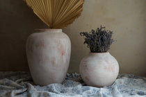 Two pottery vases exude rustic beauty on a patterned cloth; the larger terracotta vase holds a dried palm leaf, while the smaller vase cradles dried lavender.