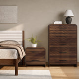 A bedroom with a matching 5-drawer wood storage vertical chest topped with a lamp against a beige wall.