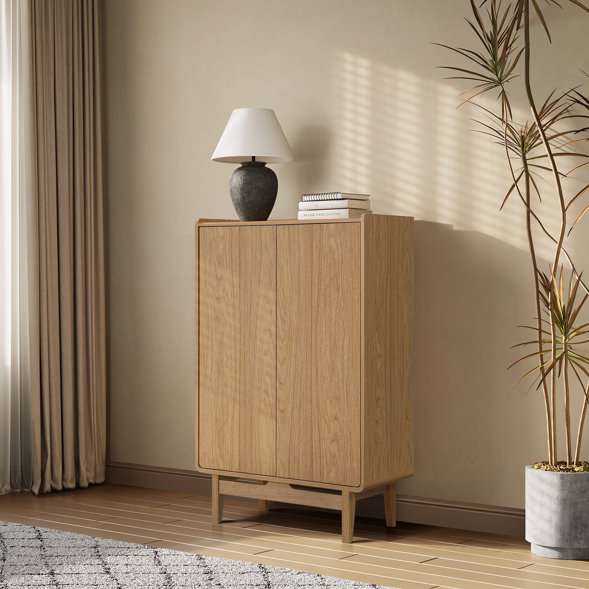 Modern light oak wood storage cabinet stands against a beige wall beside a tall plant and a window with curtains.