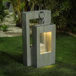 Modern outdoor water fountain with a rectangular design and LED light shines as water flows from the top into a lit lower basin, set on green artificial grass with plants in the background—perfect for enhancing any outdoor living space.