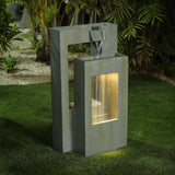 Modern outdoor water fountain with a rectangular design and LED light shines as water flows from the top into a lit lower basin, set on green artificial grass with plants in the background—perfect for enhancing any outdoor living space.
