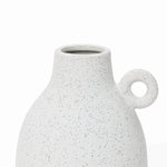 A speckled white ceramic vase with a round handle on one side, featuring a wide opening at the top and showcasing a vintage-inspired design.