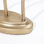 Close-up of a metallic gold-colored candle holder with an elegant design, featuring two vertical rods attached, resting on a flat white surface. Perfect for enhancing your home decor.