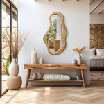 Modern room with a pine frame wooden console table, organic decor like decorative vases, and an abstract mirror. Large windows channel natural energy from the outdoor area with stone walls. A bedroom is partially visible in the background.