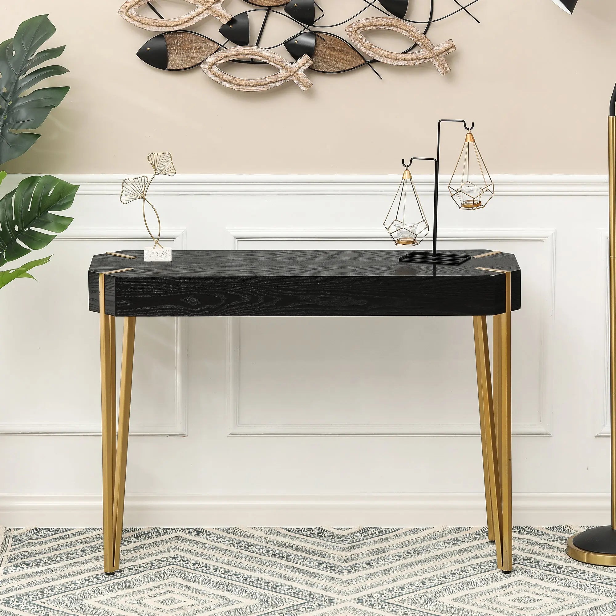 A modern console table with a black tabletop and striking metal hairpin legs sits against a white paneled wall, styled with minimalist decor and accented by fish-shaped wall art above it.