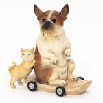 An eclectic style decor piece features a French bulldog statue crafted from clay, perched on a wooden skateboard with wheels. Beside it, a smaller clay cat leans casually, adding charm to this playful scene.