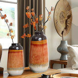 Two decorative vases with orange and gray hues, featuring a color block gradient, contain branches with orange blossoms. They rest on a wooden table in a modern, neutral-toned room, adding charm to your homes decor.
