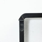 Close-up of a black, triangular metal bracket with two screws on a white wall, designed as part of a wall-mounted coat rack with flip-down hooks, securely connecting two metal pieces at a right angle.