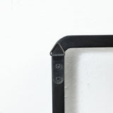 Close-up of a black, triangular metal bracket with two screws on a white wall, designed as part of a wall-mounted coat rack with flip-down hooks, securely connecting two metal pieces at a right angle.