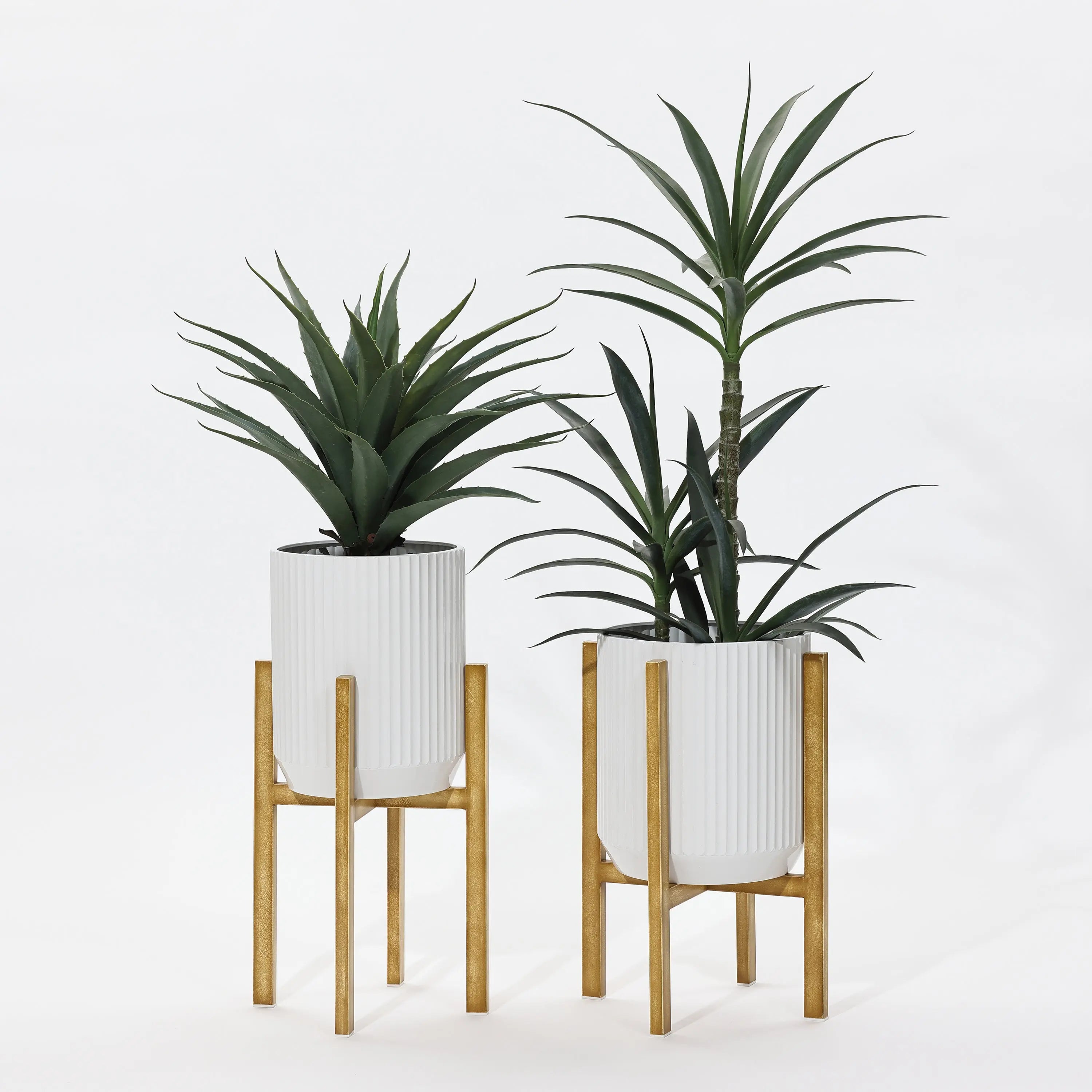 Two tall potted plants in sleek, modern metal plant pots feature white ribbed designs on wooden stands against a plain white background.