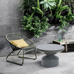 A modern patio with a green metal chair, yellow cushion, contemporary round coffee table in a gray finish, wooden bench, glassware, and a wall planter with succulents and greenery.
