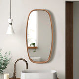 A modern wall mirror with an oval wooden frame hangs on a white wall above the sink, accompanied by a white pendant light and a planter brimming with greenery.