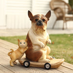 A durable resin French bulldog statue sits on a skateboard, with a ceramic cat playfully leaning against it outdoors on a wooden patio. In the eclectic style decor scene, a wicker chair and grass are in the background.