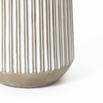 Close-up of a beige and white ceramic vase with vertical ribbed texture, resembling a striped planter, partially visible against a white background.