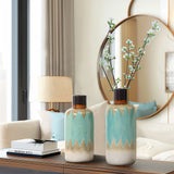 Two coastal-inspired ceramic vases with blue and beige patterns hold branches with white flowers. They sit on a wooden surface near a mirror in a modern room, adding nautical charm to the elegant space.
