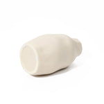 An ivory white, rounded ceramic vase lies elegantly on its side against a plain white background, serving as a minimalist accent piece.
