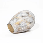 A speckled, oval-shaped ceramic vase with a muted color palette lies on its side against a white background, evoking a broken egg design.