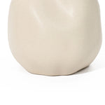 A smooth, matte beige ceramic vase with an irregular, rounded shape serves as a stunning accent piece against the ivory white background.