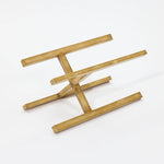 A brass-colored metal stand with a geometric, angular design featuring intersecting rods offers lightweight construction, making it perfect for supporting modern metal plant pots.