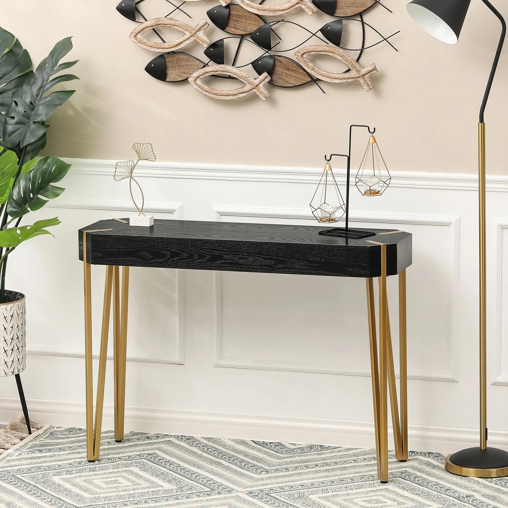 A modern black console table with metal hairpin legs sits against a wall, decorated with metal sculptures and positioned beside a floor lamp and green plant.