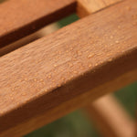 A close-up of rain droplets glistens on the wooden slats of an outdoor bench, highlighting its solid wood construction.