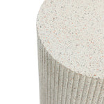Close-up of a textured, cylindrical ivory white side table with a speckled surface and vertical ridges, crafted from durable cement material.