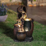 A rustic urn outdoor fountain featuring three jugs and an LED light in the illuminated basin, set on grass in a garden at dusk—an inviting piece of garden decor.