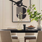 This elegant dining room features a black table, beige chairs, and a sophisticated candle holder. A bowl of pears and a vase with green branches add charm, while abstract art and a chandelier complete the exquisite home decor.