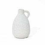 A speckled white ceramic vase with a handle on a white background, this vintage-inspired piece adds charm to any home decor setting.