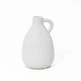 A speckled white ceramic vase with a handle on a white background, this vintage-inspired piece adds charm to any home decor setting.