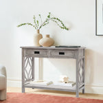 A modern farmhouse console table in distressed gray wash with two drawers stands against a white wall, decorated with neutral vases holding branches, a tray, and books on the spacious lower shelf.